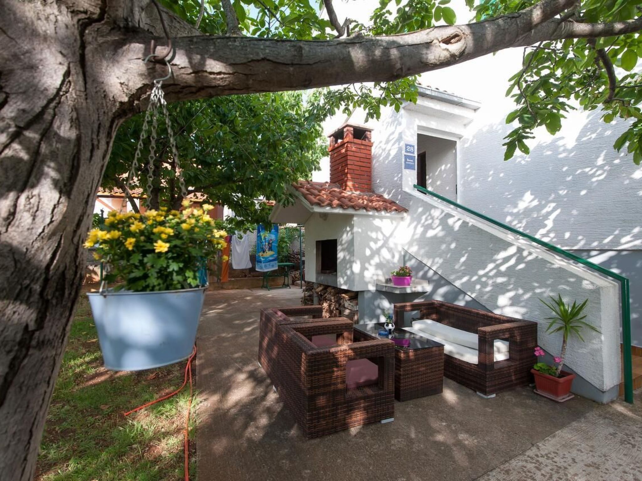 Um pátio com móveis de vime, plantas pendentes e um edifício branco com telhado de telhas vermelhas.