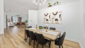 A modern dining area with a wooden table, black chairs, and a ceiling fan. - South Cape Luxury | Putt Green, HTD POOL,& Game RM (Cape Coral)