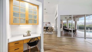 A modern kitchen with wooden cabinets, a white countertop, and a black chair. - South Cape Luxury | Putt Green, HTD POOL,& Game RM (Cape Coral)
