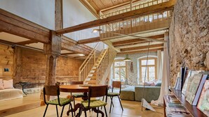 Une pièce spacieuse avec un escalier en bois, une table ronde entourée de chaises et une bibliothèque remplie de livres.