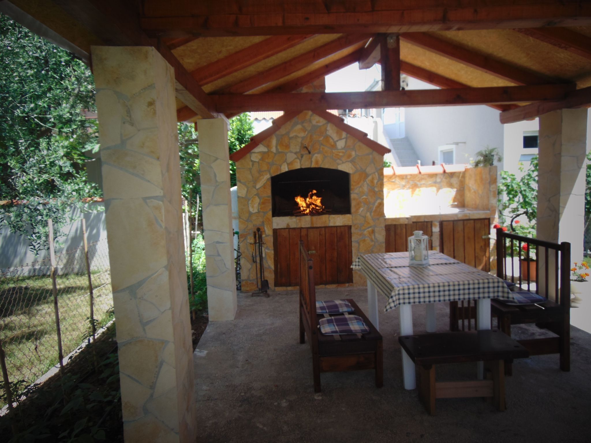 Eine Terrassengaststätte mit Kamin aus Stein, Holztisch und -stühlen und Blick auf den umliegenden Garten.