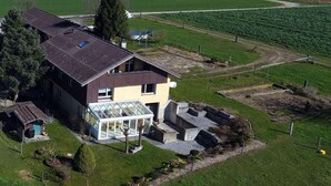 Une maison à deux étages dotée d’une grande véranda en verre, entourée d’une pelouse bien entretenue et d’un champ.
