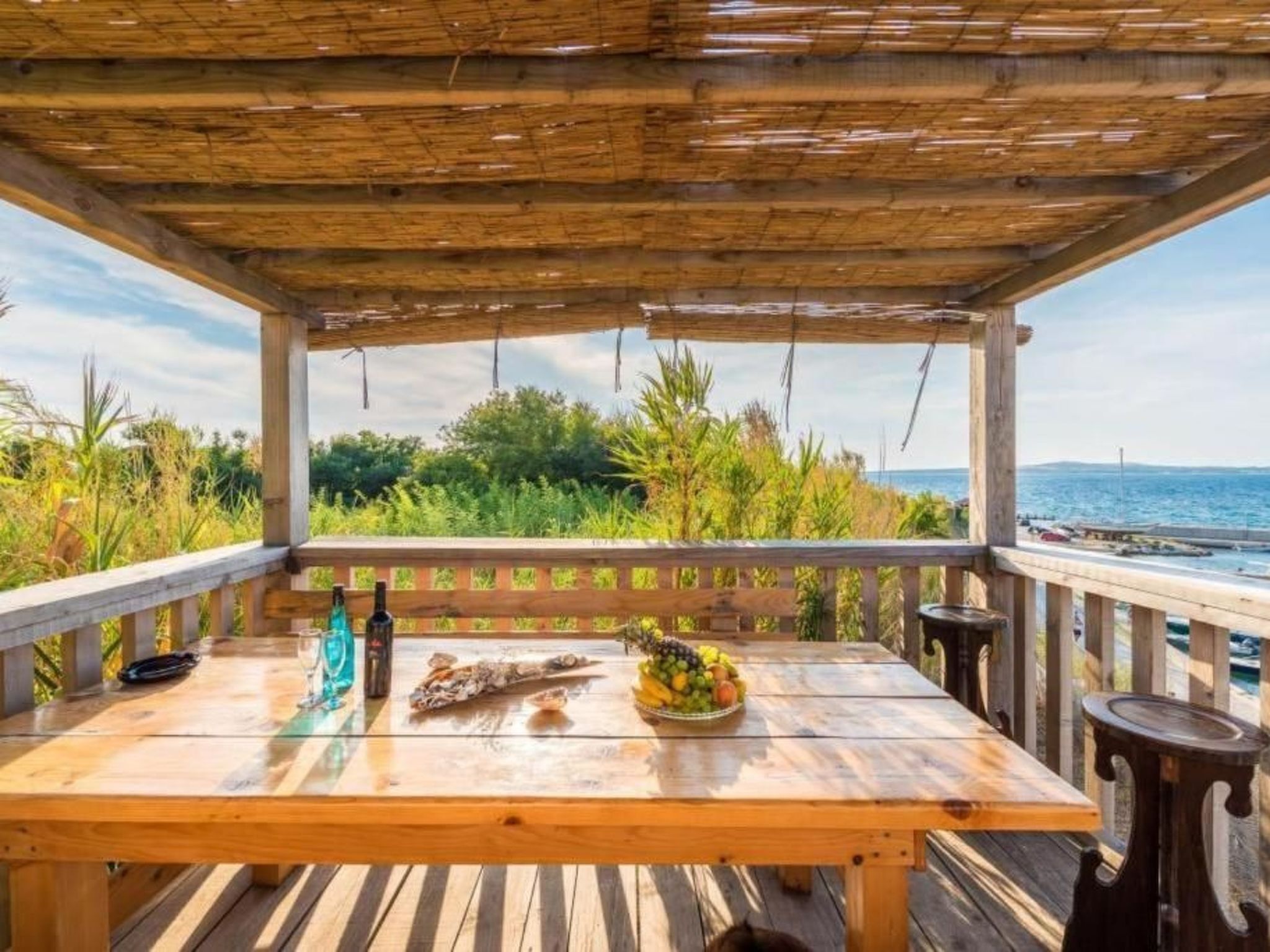 Eine Holzterrasse mit gedecktem Tisch, mit Blick auf ein Gewässer und viel Grün.
