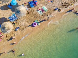 Luchtbeeld van een strand met parasols, ligbedden en mensen die van het zand en de zee genieten.