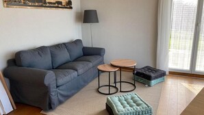 A modern living room with a grey sofa, two round wooden tables, a black floor lamp, and a cushioned ottoman. - Apartment Seehof by Interhome (Rorschacherberg)