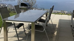 An outdoor patio with a table and chairs, a grill, and a view of the sea and cityscape. - Apartment Seehof by Interhome (Rorschacherberg)