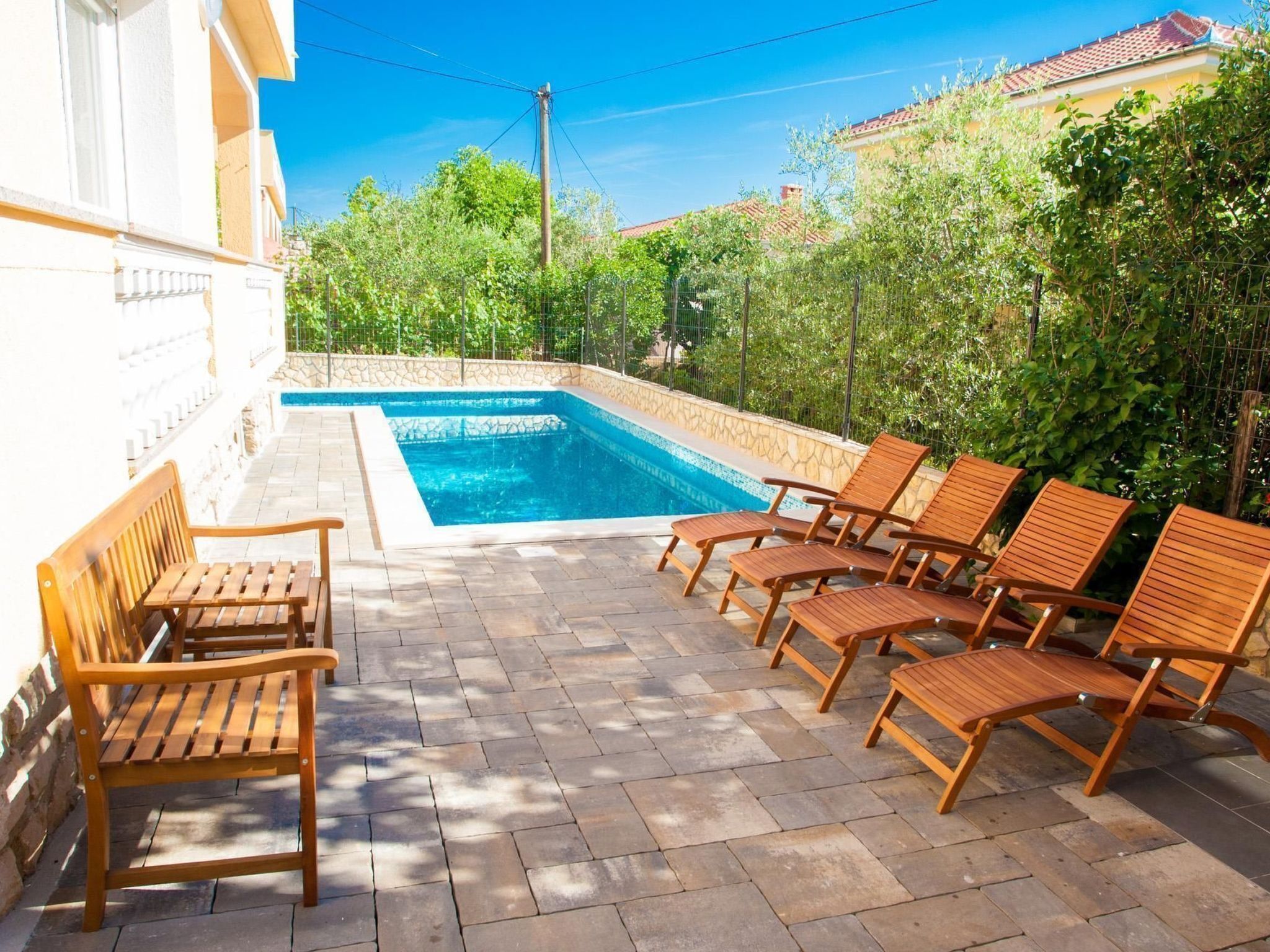 A swimming pool with wooden loungers and a stone-tiled patio area.
