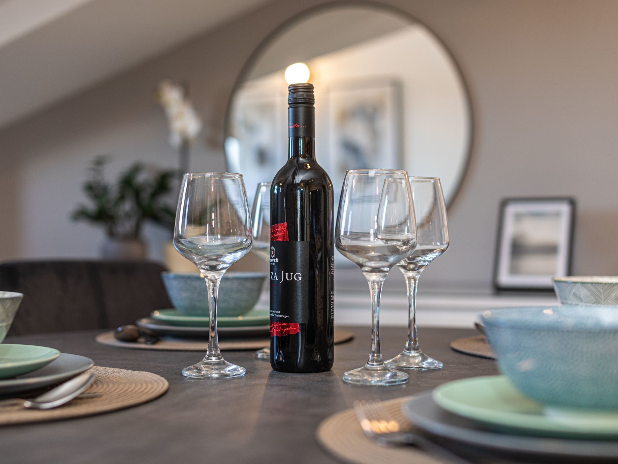 A bottle of wine, two empty wine glasses, and a bowl on a table.