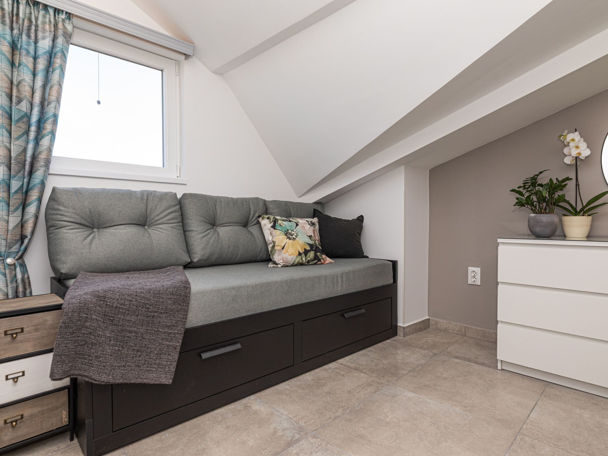 A modern loft bedroom with a built-in sofa bed, a dresser, and a potted plant.