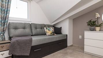 A modern loft bedroom with a built-in sofa bed, a dresser, and a potted plant.