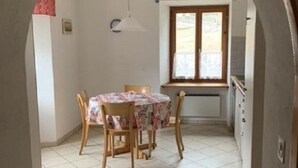 Een eetgedeelte met een tafel, stoelen, een raam met gordijnen en een betegelde vloer.