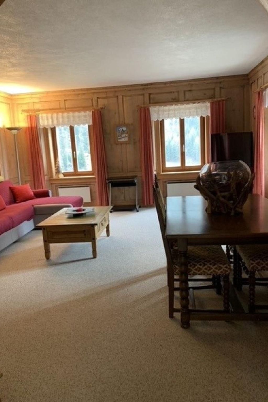 Un accogliente soggiorno con arredamento in legno, un divano, un tavolino, un tavolo da pranzo con sedie e un vaso grande.