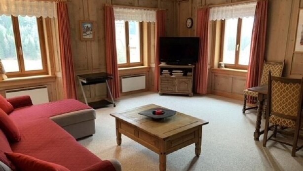 Een gezellige woonkamer met een bank, een salontafel, een televisie en een eethoek met een stoel.