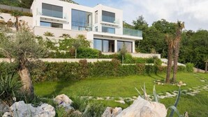 Una casa moderna de dos pisos con amplios ventanales, un balcón y un jardín cuidado con rocas y plantas.