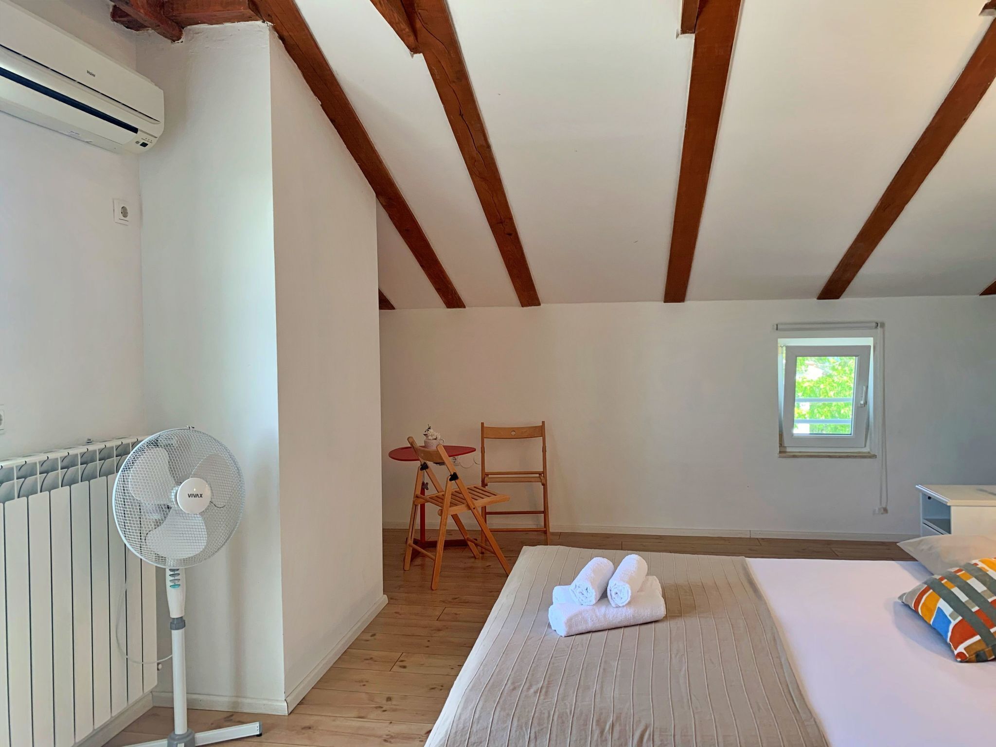A room with a bed, a fan, a table with chairs, a window, and a radiator.