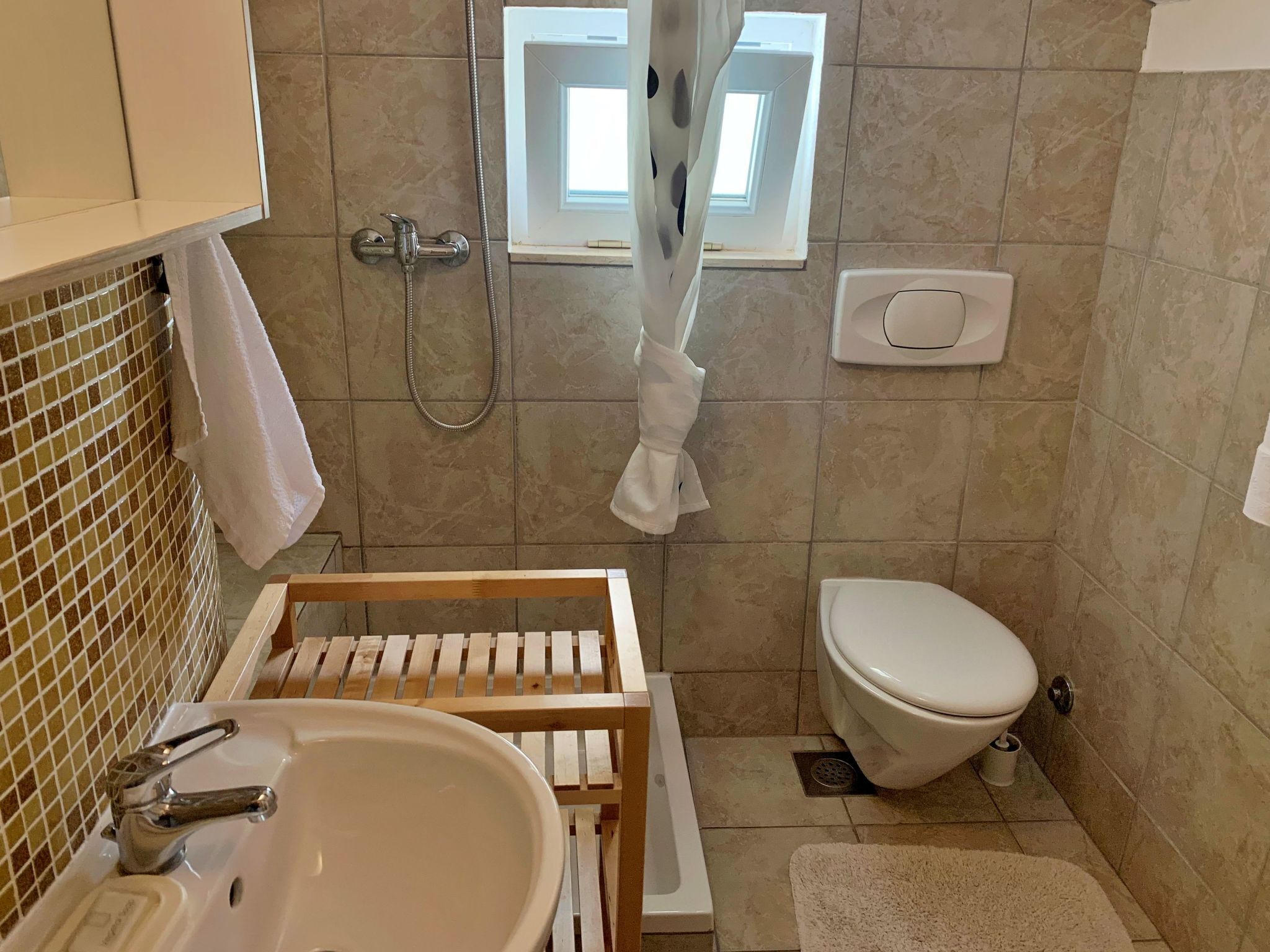 A bathroom with a sink, toilet, shower, and a window.