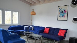 Un salon moderne avec un canapé bleu, deux tables basses en verre, une lampe sur pied et un tableau abstrait encadré accroché au mur.