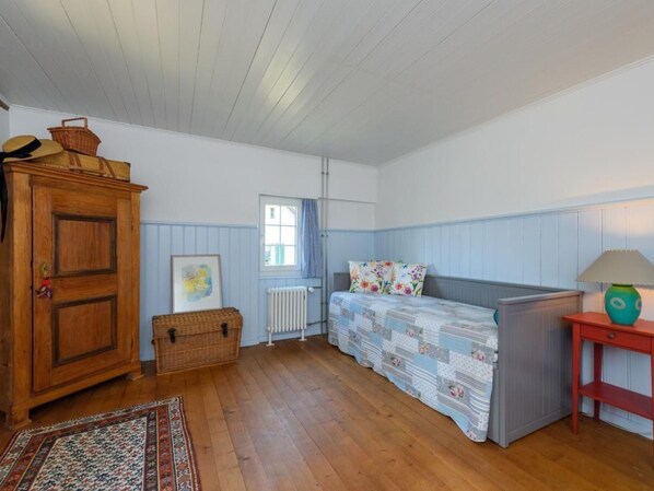 Una habitación acogedora con un armario de madera, una cesta de mimbre, una cama con ropa de cama floral, una mesita de noche roja y una alfombra estampada.