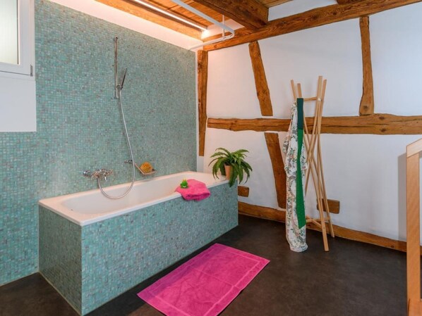A bathroom with a bathtub, a shower, a pink towel, a potted plant, and wooden beams.