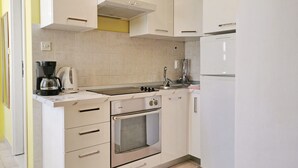 Una cucina compatta con mobili bianchi, forno integrato, piano cottura, lavello e macchina per caffè.