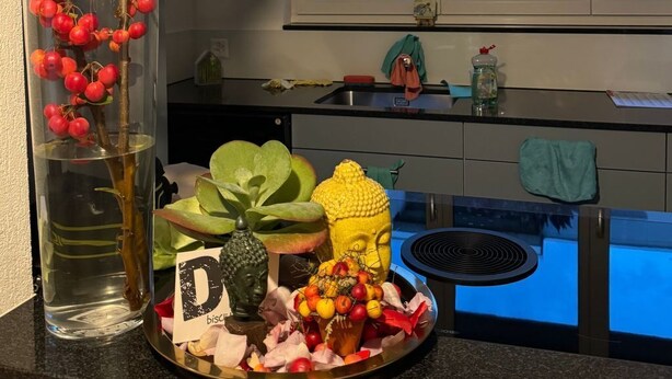 En køkkenbordplade med frugt, en Buddha-figur og en dekorativ vase.