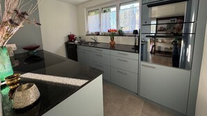Et moderne køkken med grå skabe, en sort bordplade og et rustfrit stål køleskab.