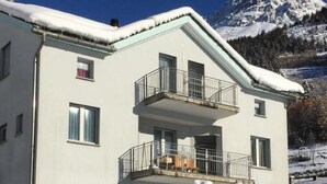 Un bâtiment à deux étages doté d’un balcon, entouré de neige et avec des montagnes en arrière-plan.
