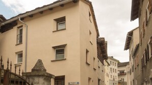 Une étroite rue pavée bordée de bâtiments traditionnels, avec une porte en pierre et une enseigne indiquant un espace public.