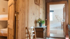 Une pièce rustique en bois, avec un lit superposé, une chaise en bois et un bureau agrémenté d’une plante en pot.