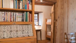 Une pièce chaleureuse avec une bibliothèque en bois remplie de livres, une commode ornée de motifs en dentelle, un lit superposé en bois et une chaise.