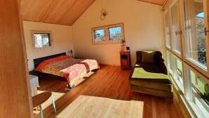 A cozy attic bedroom with a wooden ceiling, a bed with a patterned bedspread, a green sofa, and large windows offering a view of the outdoors.