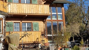A wooden chalet with a balcony, large windows, and a wooden deck.