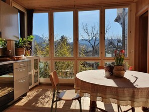 A kitchen with a dining table and chairs, large windows with a view of trees and mountains, and potted plants on the windowsill. - im ruhigen Berner Gartenquartier by Interhome (Liebefeld)