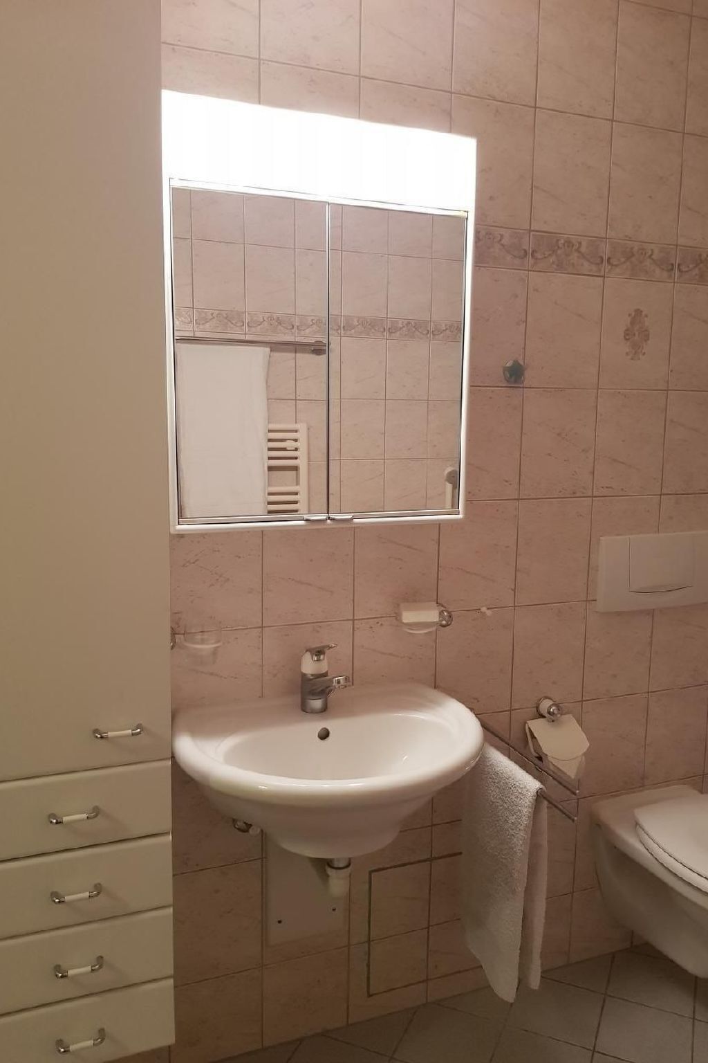 A bathroom with a white sink, a mirror, a toilet, and a cabinet with drawers.