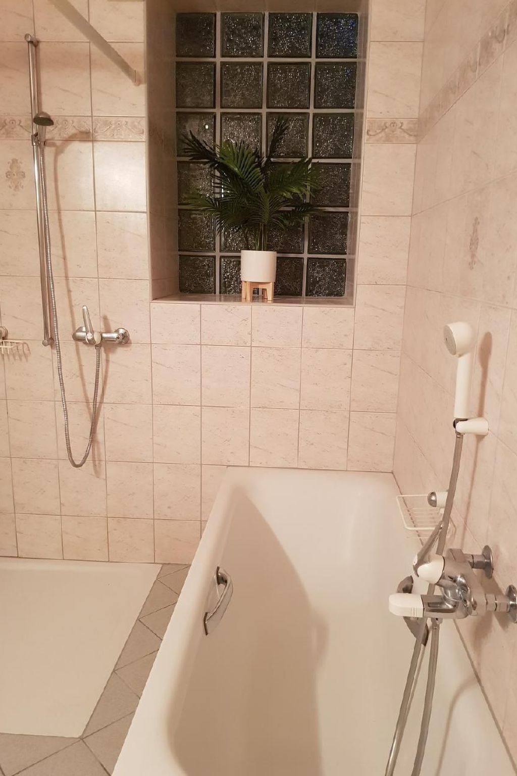 A bathroom with a bathtub, a shower area, and a window with a plant.