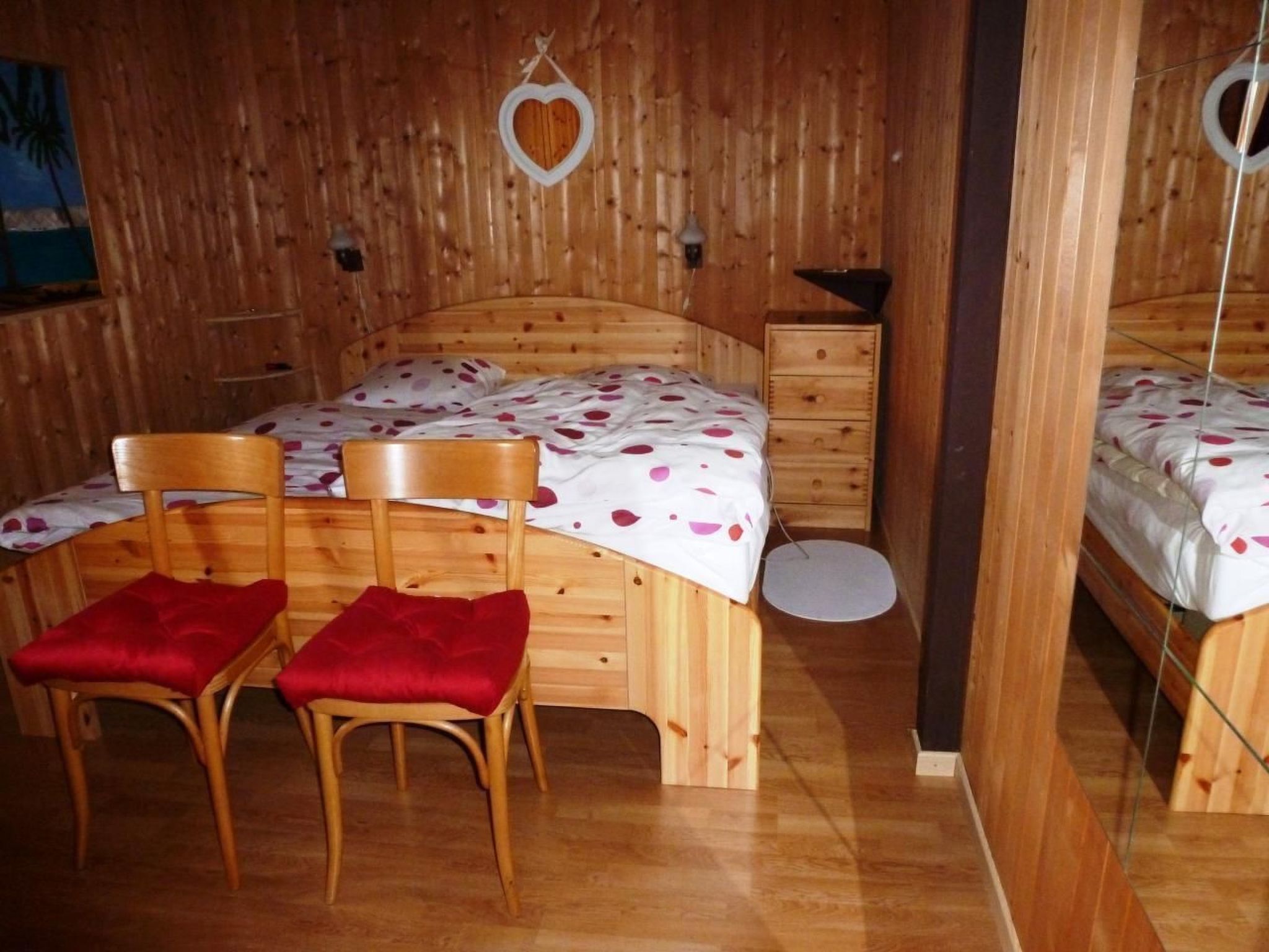 Una stanza in legno con un letto, due sedie, una cassettiera e uno specchio.