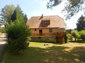 Ein zweistöckiges Haus mit einem Ziegeldach, einem Balkon mit Holzbalkonen und einer Steinmauer.