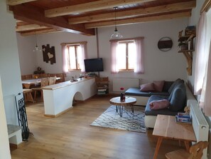 Ein gemütliches Wohnzimmer mit Holzboden, einer Couch, einem Fernseher und einem Essbereich mit Tisch und Stühlen.