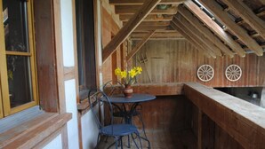 Ein Zimmer mit Holzeinrichtung, einem Tisch, Stühlen, einem Fenster mit Vorhang und einer Holzbalkendecke.