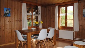 Ein Esszimmer mit Holzboden, einem Tisch, Stühlen, einer Hängeleuchte und einem Fenster mit Vorhängen.