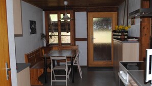 Eine kleine Küche mit Holztisch, Sitzbank, Herd und einer Tür mit Milchglasscheiben.