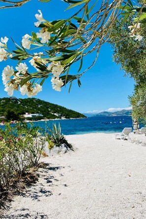 Ein Strand mit weißem Sand, einem klaren blauen Meer und einem grünen Hügel in der Ferne.