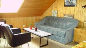 A cozy room with a wooden ceiling, a blue sofa, a small table, and a chair.