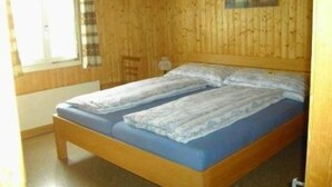 A wooden-paneled room with a bed, a window with curtains, and a picture on the wall.