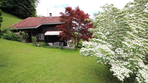 Ein rustikales Haus mit rotem Ziegeldach, umgeben von einem gepflegten Rasen und einem blühenden Baum.