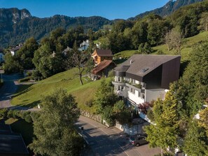 Ein modernes, zweistöckiges Haus mit geneigtem Dach, umgeben von üppiger Vegetation und einer Berglandschaft.