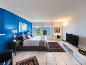 Ein modernes Schlafzimmer mit einem großen Bett, einem Flachbildfernseher und Blick ins Freie.