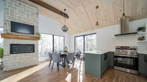 Eine moderne Küche mit Kamin aus Stein, großen Fenstern und einem Essbereich mit Holzboden.