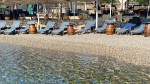Uma praia com águas calmas e transparentes, cadeiras de praia e guarda-sóis.