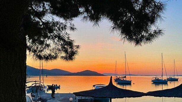 Uma área à beira-mar com barcos, um espaço de estar coberto e vista para o pôr do sol sobre a água.